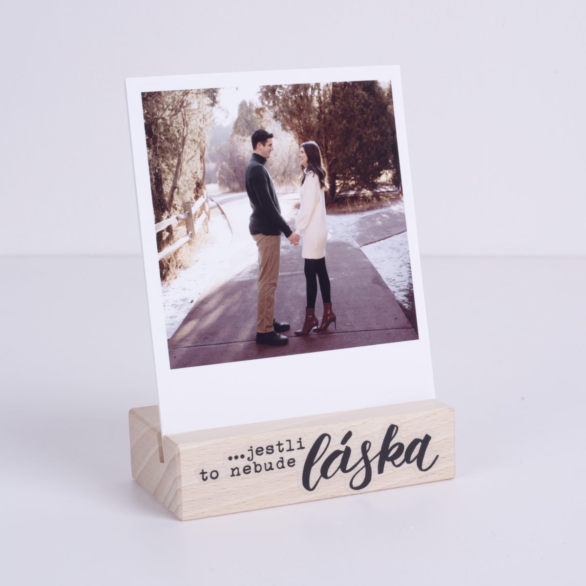 Série polaroidek s fotkami zamilovaného páru v dřevěném stojánku, který je vyzdobený samolepkami.